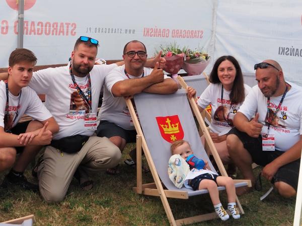 na zdjęciu znajduje się sześć osób, w tym jedna to mały chłopiec poniżej 2 lat. Chłopiec leży na leżaku z herbem, a za nim...